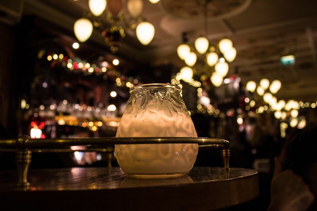 Trago servido sobre barra de madera con luces cálidas de fondo